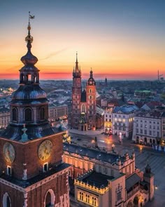 an aerial view of a city at dusk with the sun setting in the distance and buildings lit up
