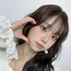 a woman with long dark hair wearing a white dress and holding her hand on her head