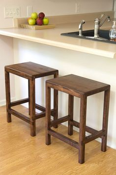 two wooden stools sitting on top of a hard wood floor next to a counter