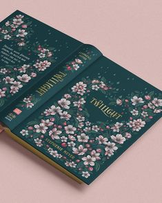 an open book with floral designs on the front and back cover, sitting on a pink surface