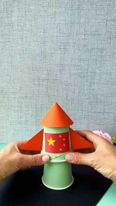 two hands are holding up a paper toy with a red and yellow star on it