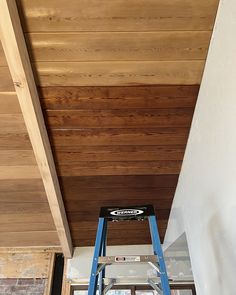 a man on a ladder painting the ceiling in a house that is being renovated with wood paneling
