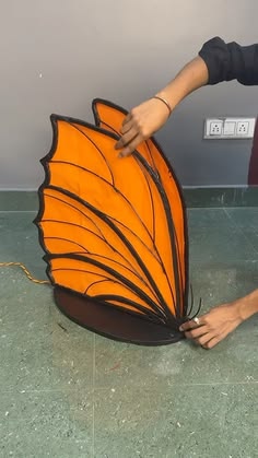 a person touching the side of a large orange butterfly shaped object with its wings spread out
