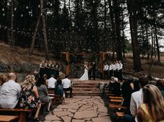 a wedding ceremony in the woods with people sitting on benches and looking at each other
