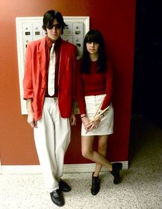two people standing next to each other in front of a red wall with an electrical outlet