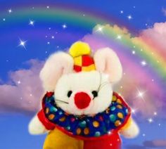 a stuffed animal with a clown hat and rainbow in the background