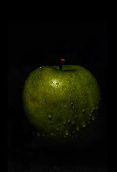 a green apple with water drops on it's surface, in the dark background