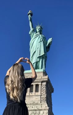 a woman standing in front of the statue of liberty with her hands up to the sky