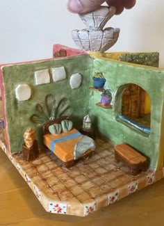 a hand is reaching into a miniature house made out of clay
