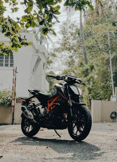 an orange and black motorcycle parked in front of a white building with trees around it
