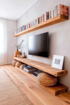 a flat screen tv sitting on top of a wooden shelf next to a wall filled with books