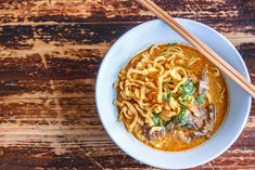 a white bowl filled with noodles and meat next to chopsticks on a wooden table