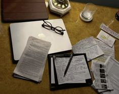 an open laptop computer sitting on top of a wooden desk covered in papers and paperwork