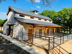 a horse barn with a metal roof and two stalls on each side, surrounded by trees