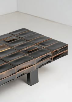 a table made out of black and gold tiles on top of a white floor next to a wall