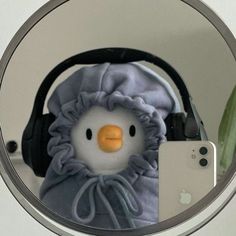 a stuffed penguin with headphones is in front of a mirror that has a cell phone on it