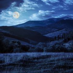 the full moon shines brightly in the sky over a grassy field and mountain range