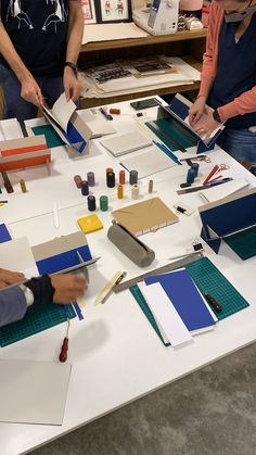 three people are working on crafts at a table with paper and glues in front of them