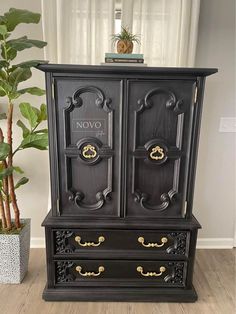 an ornate black armoire with gold handles in front of a potted plant and window
