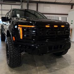 a black truck parked in a garage with its lights on and it's hood up