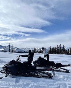 two people standing next to a snowmobile in the snow