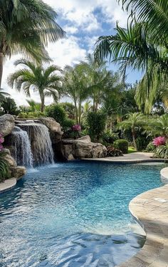 an outdoor swimming pool with waterfall and palm trees in the foreground, surrounded by lush vegetation