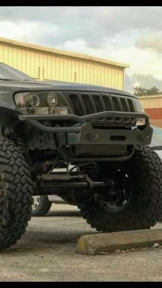 a black jeep parked in front of a building with large tires on it's wheels