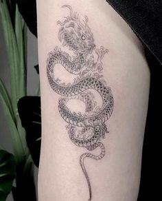 a black and white photo of a dragon tattoo on the thigh, it looks like something out of a fairy tale