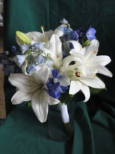 a vase filled with white and blue flowers on top of a green cloth covered table