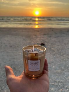 a hand holding a candle with the sun setting in the back ground behind it, on a beach