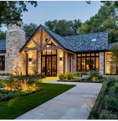 a large house with lots of windows and lights on it's front porch, surrounded by greenery