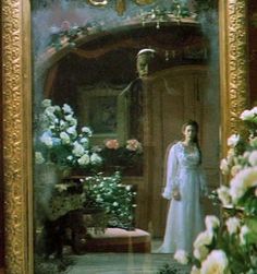 a woman standing in front of a mirror next to flowers