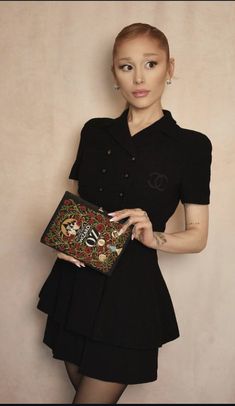 a woman in a black dress is holding a small purse and posing for the camera