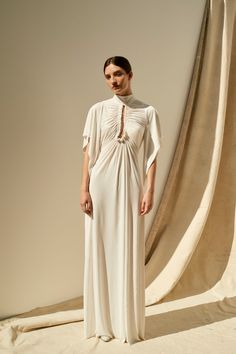 a woman standing in front of a backdrop wearing a white dress with an open neck