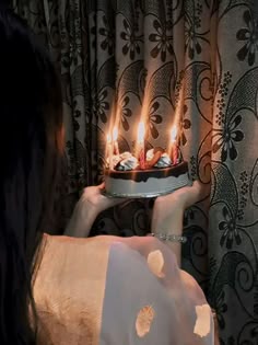 a woman holding a cake with lit candles on it
