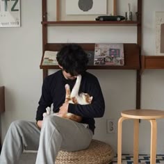 a person sitting on a stool holding a cat
