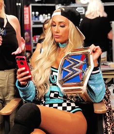 a woman sitting on top of a counter holding a cell phone and wearing a wrestling belt