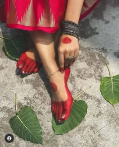 a woman's feet with red paint on them and green leaves around her ankles