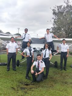 a group of people standing next to each other in front of an airplane on the grass