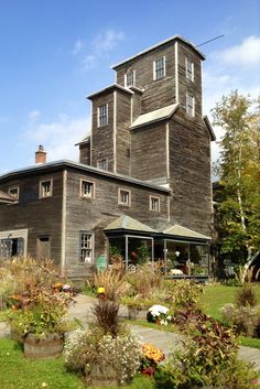 an old wooden house with lots of flowers in the front yard