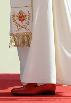 the feet of a person wearing red shoes and a white dress with gold trims