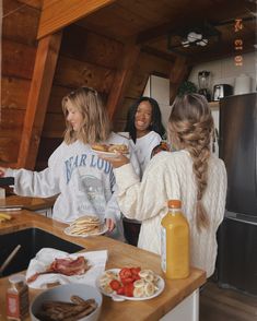 three women standing in a kitchen with food and condiments on the counter top