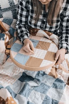a woman sitting on a bed with a cross stitch project in her lap and holding a wooden hoop