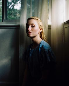 a woman standing in front of a window with her head turned to the side and eyes closed