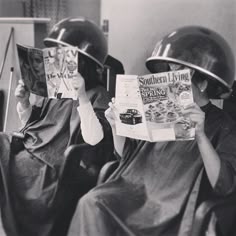 two people sitting in chairs with helmets on their heads and reading magazines while one person holds up a magazine