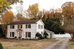 a large white house with black shutters and trees in the back ground, on a fall day