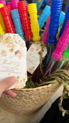 a person holding up a small card in front of some colorful straw baskets with tags on them