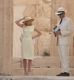 a man in a white suit and hat standing next to a woman wearing a yellow dress