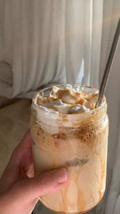 a hand holding a glass jar filled with ice cream and whipped cream on top of it