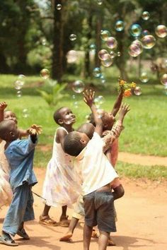 children playing with soap bubbles on a dirt road in a park, some holding flowers